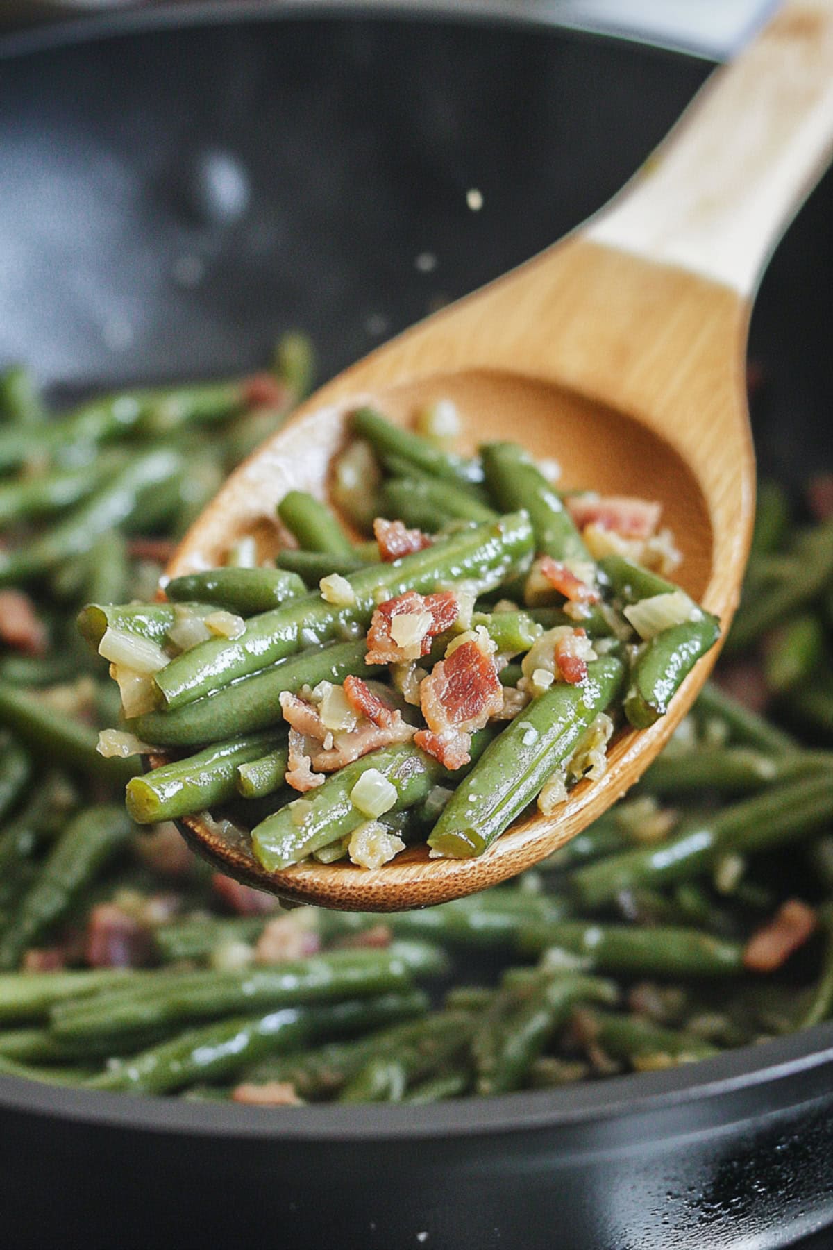 Sauteed green beans with bacon lifted by a wooden ladle from a pan.