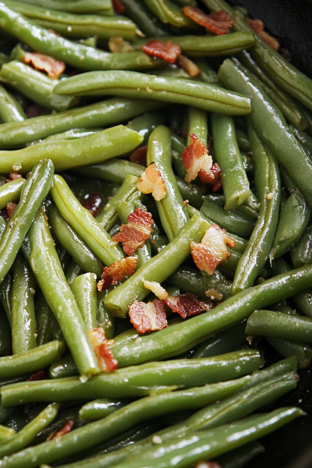 Green beans sauteed with crumbled bacon in a pan. 