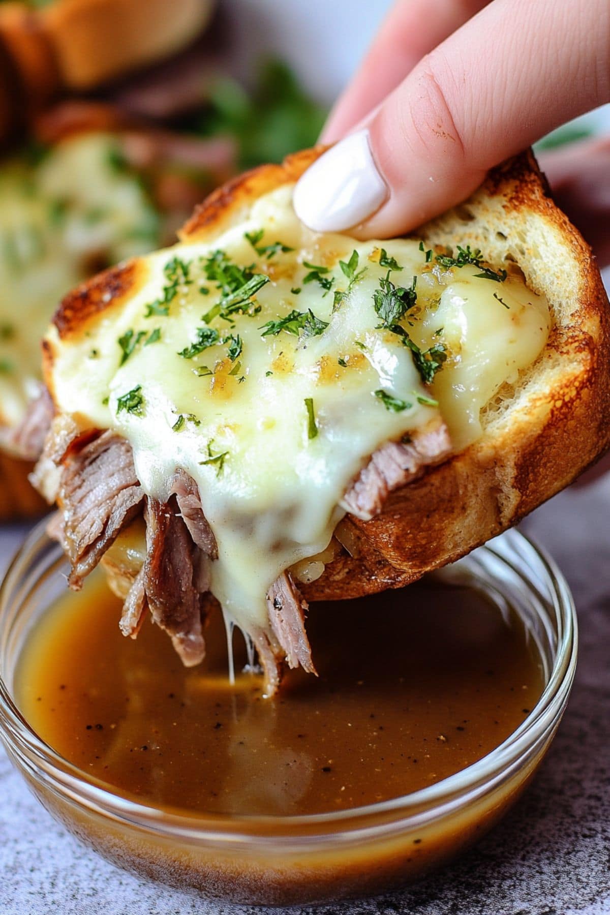 Hand holding a piece of Texas toast with cheese and beef dipping it to small bowl with gravy. 