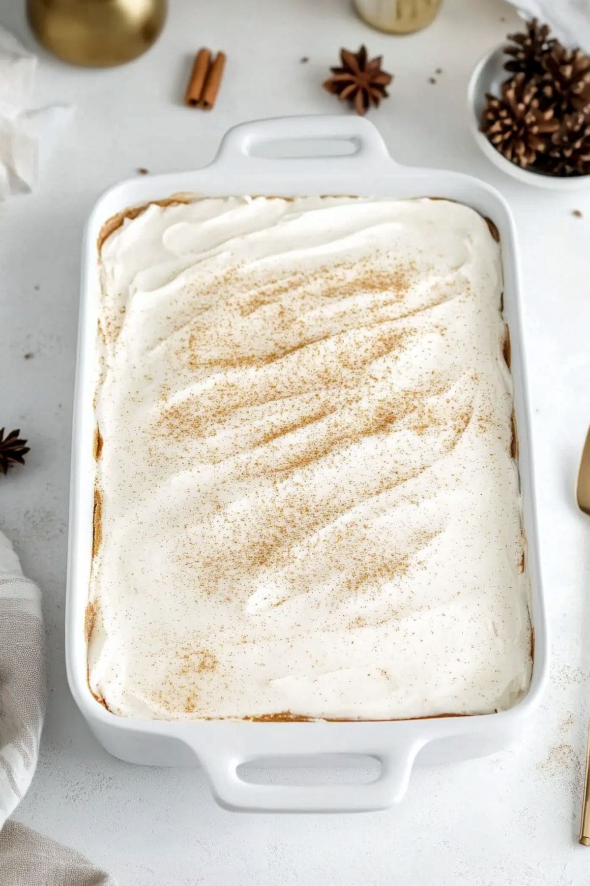 Cake in a baking dish covered with frosting, dusted with nutmeg.