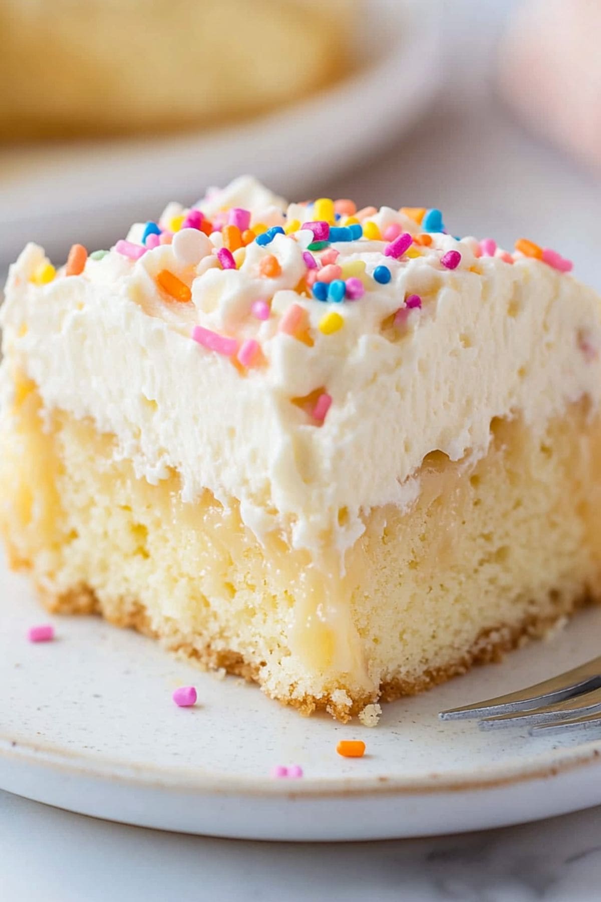 Square slice of vanilla poke cake with whipped cream on top garnished with candy sprinkles.