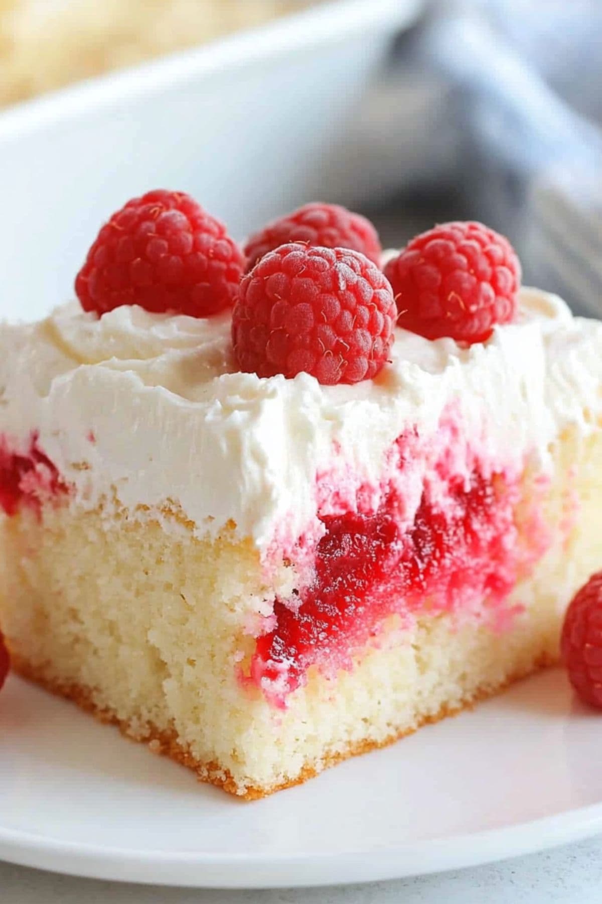 Slice of vanilla cake with red Jello streaks topped with whipped cream garnished with fresh raspberries and shredded white chocolate.