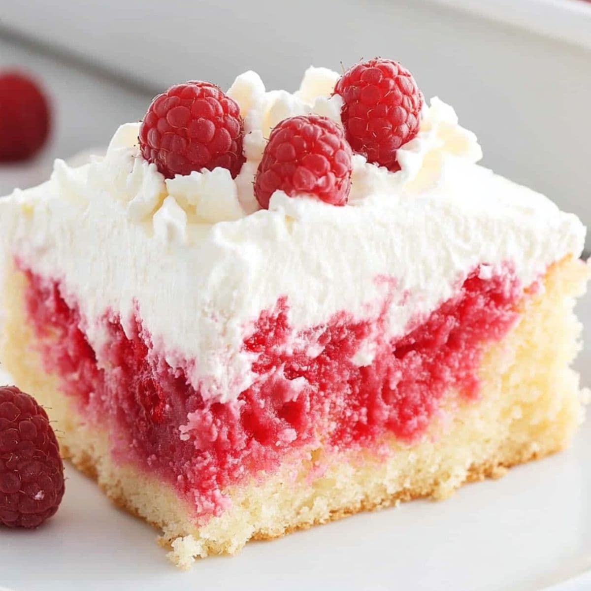 White chocolate raspberry poke cake slice garnished with raspberries and white chocolate shavings served in a white plate.