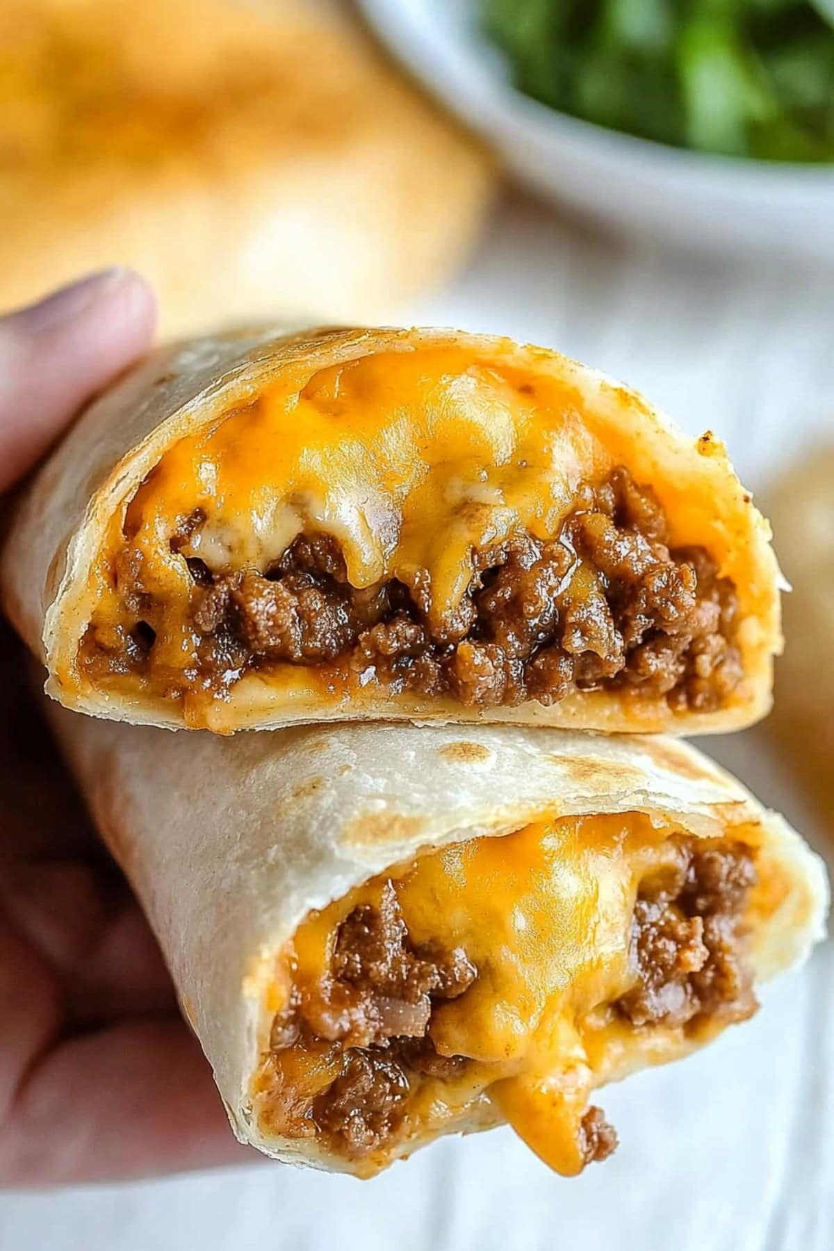 A hand holding two ground beef and cheese chimichangas