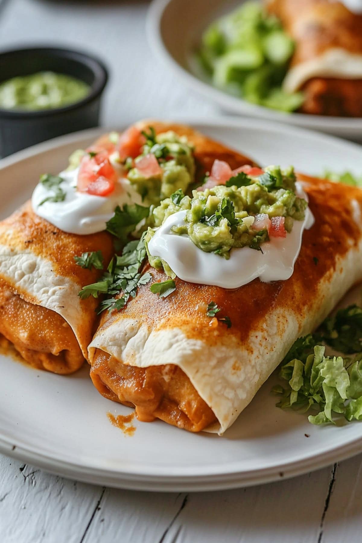 A plate of homemade chimichangas filled with ground beef and cheese, topped with sour cream and guacamole.