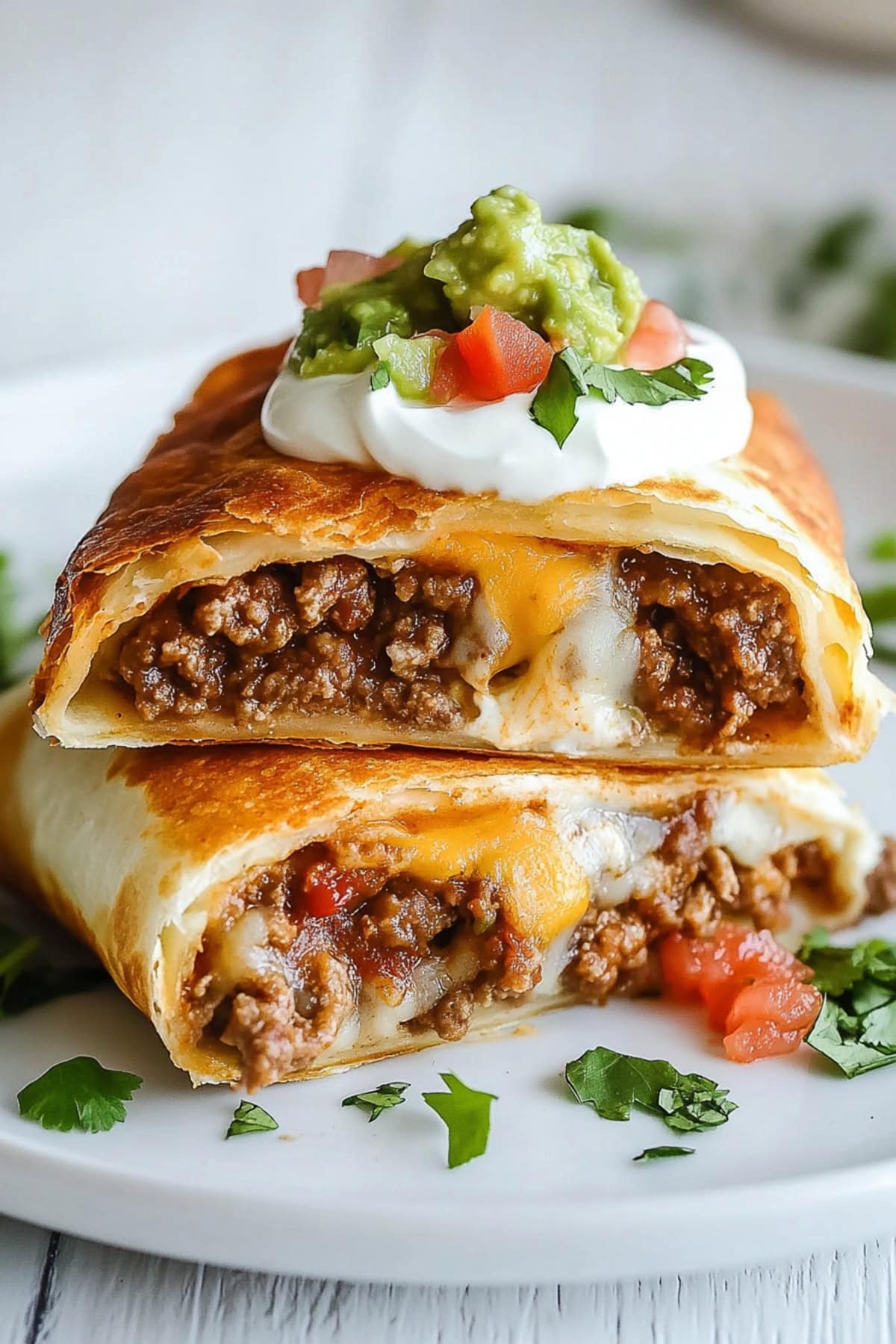 Chimichangas with melty cheese and beef, topped with sour cream and guacamole, side view