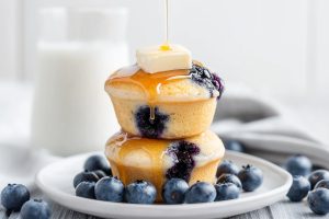 Blueberry pancake muffins stacked on top of each other with butter, drizzled with maple syrup.