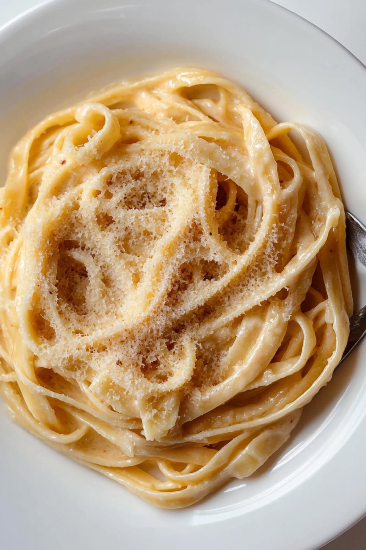 Serving of creamy brown buttered fettucine alfredo served in a white plate.