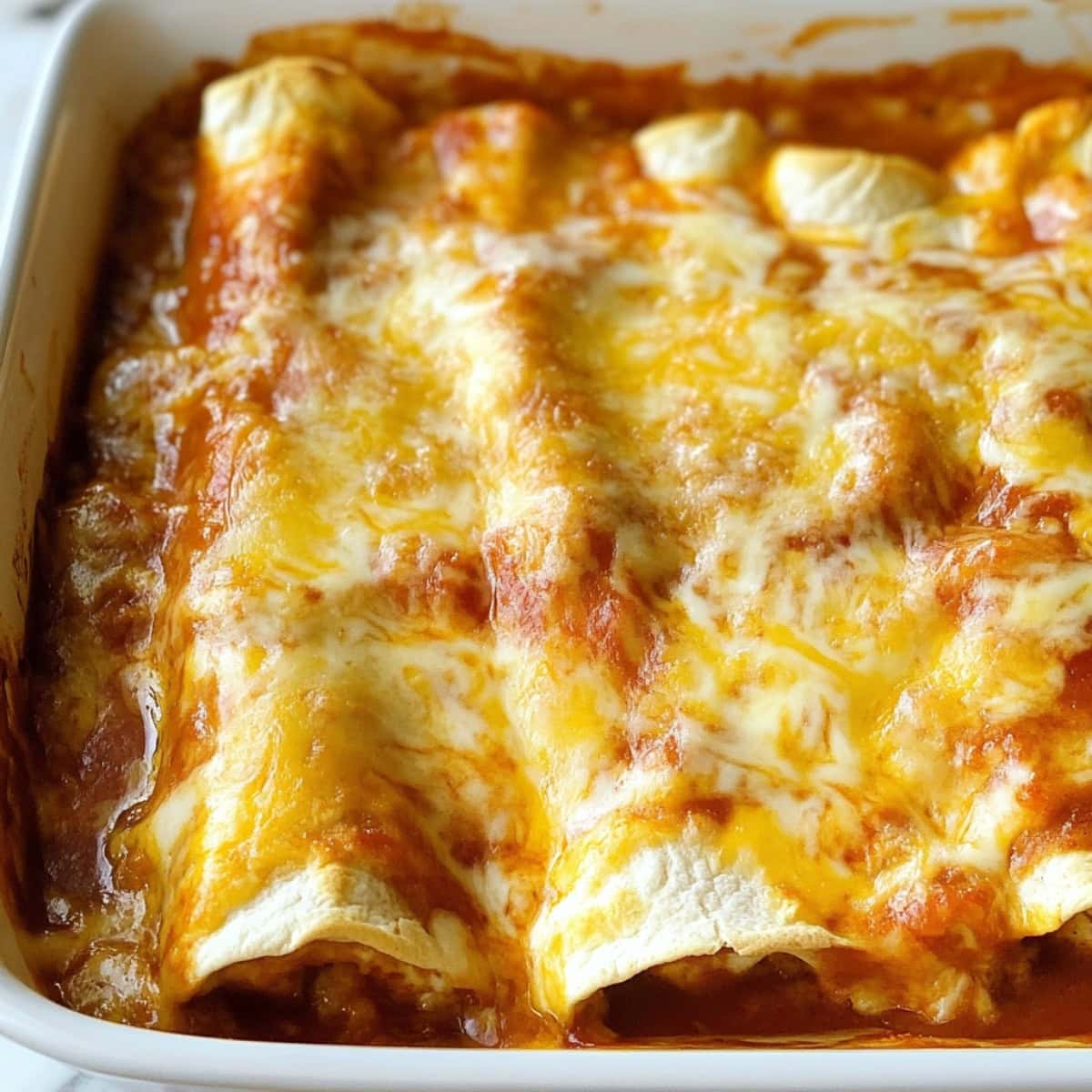 Cheesy enchiladas in a baking dish topped with red sauce gooey cheese.