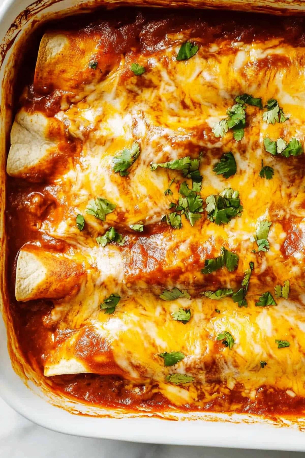 Cheesy enchiladas in a baking dish garnished with chopped onions on top.