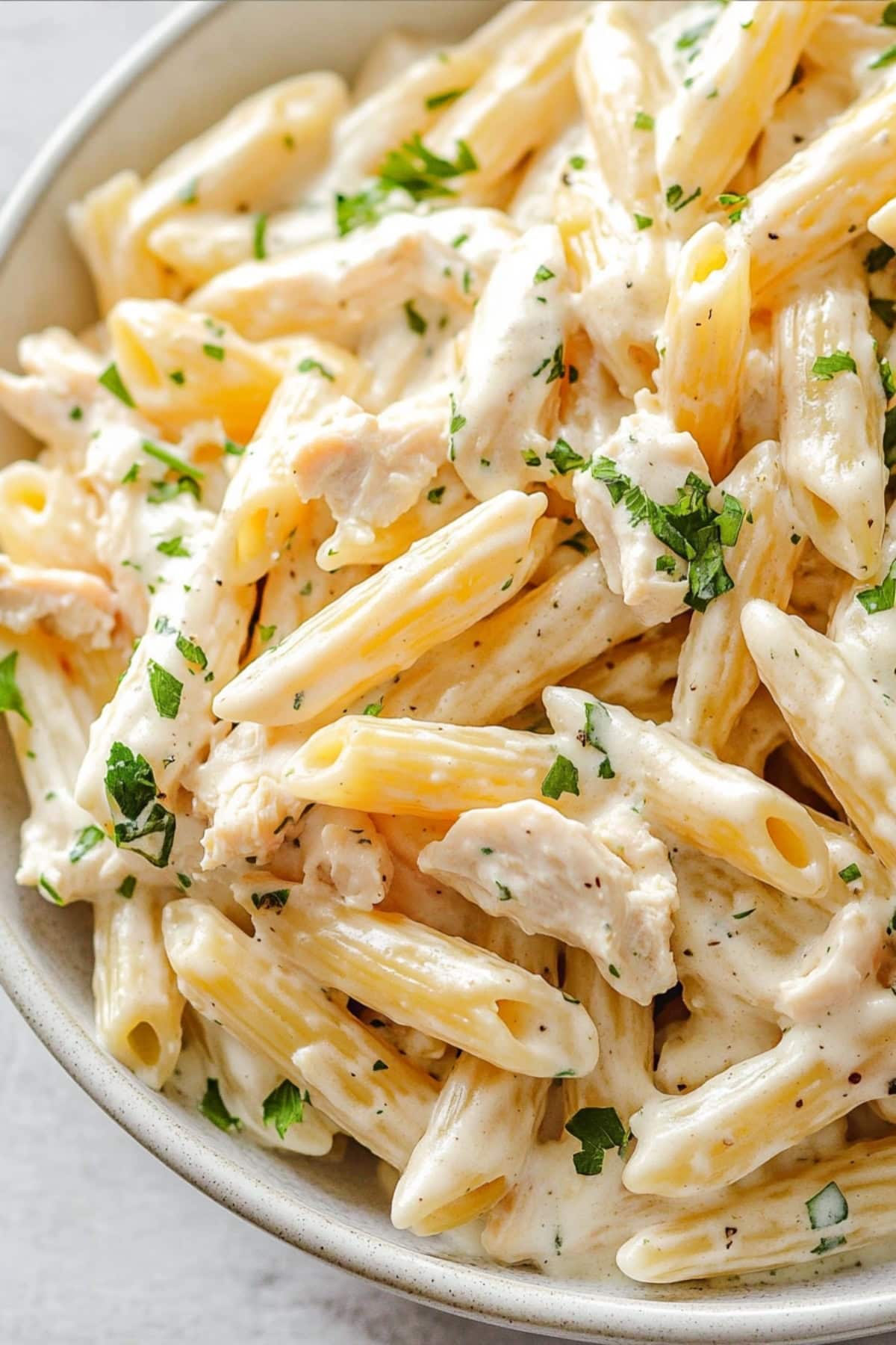 Creamy penne pasta with chicken served in a white bowl.