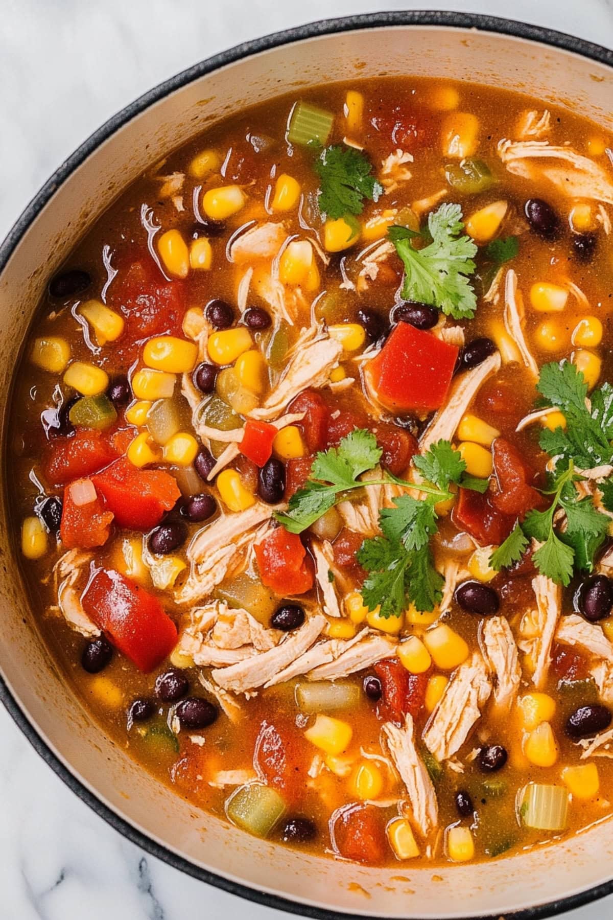 Chicken taco soup in a white pot with shredded chicken, corn, black beans in a tomato broth. 