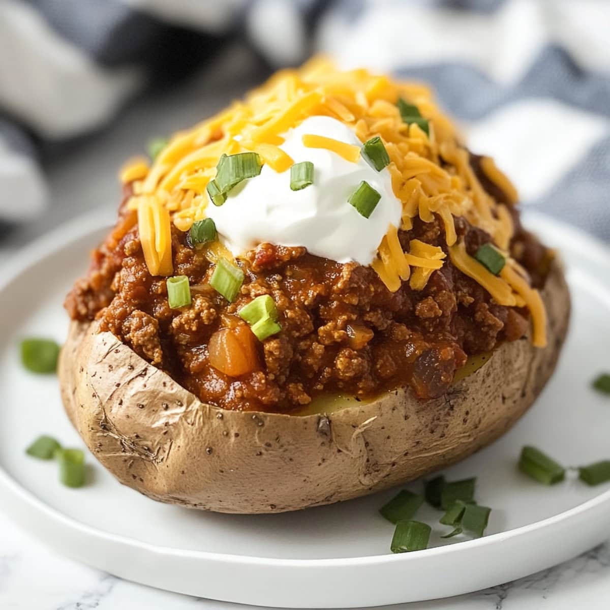 A close-up of chili baked potatoes with sour cream, chopped onions and shredded cheese in a plate.