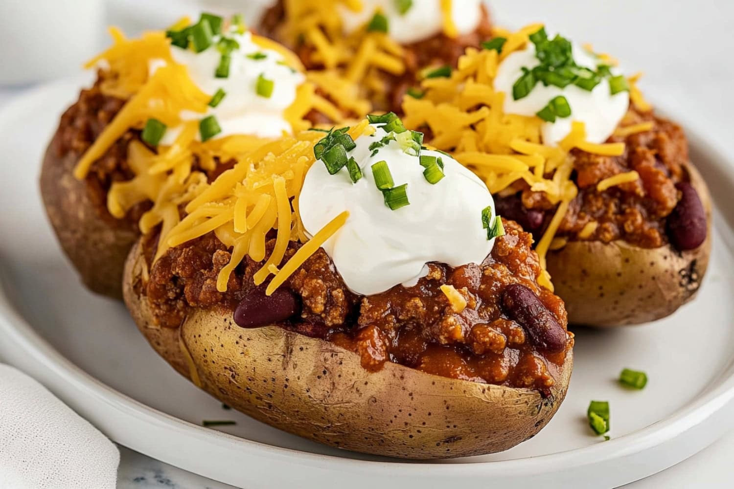 Chili baked potatoes featuring ground beef and beans, garnished with shredded cheese and sour cream.