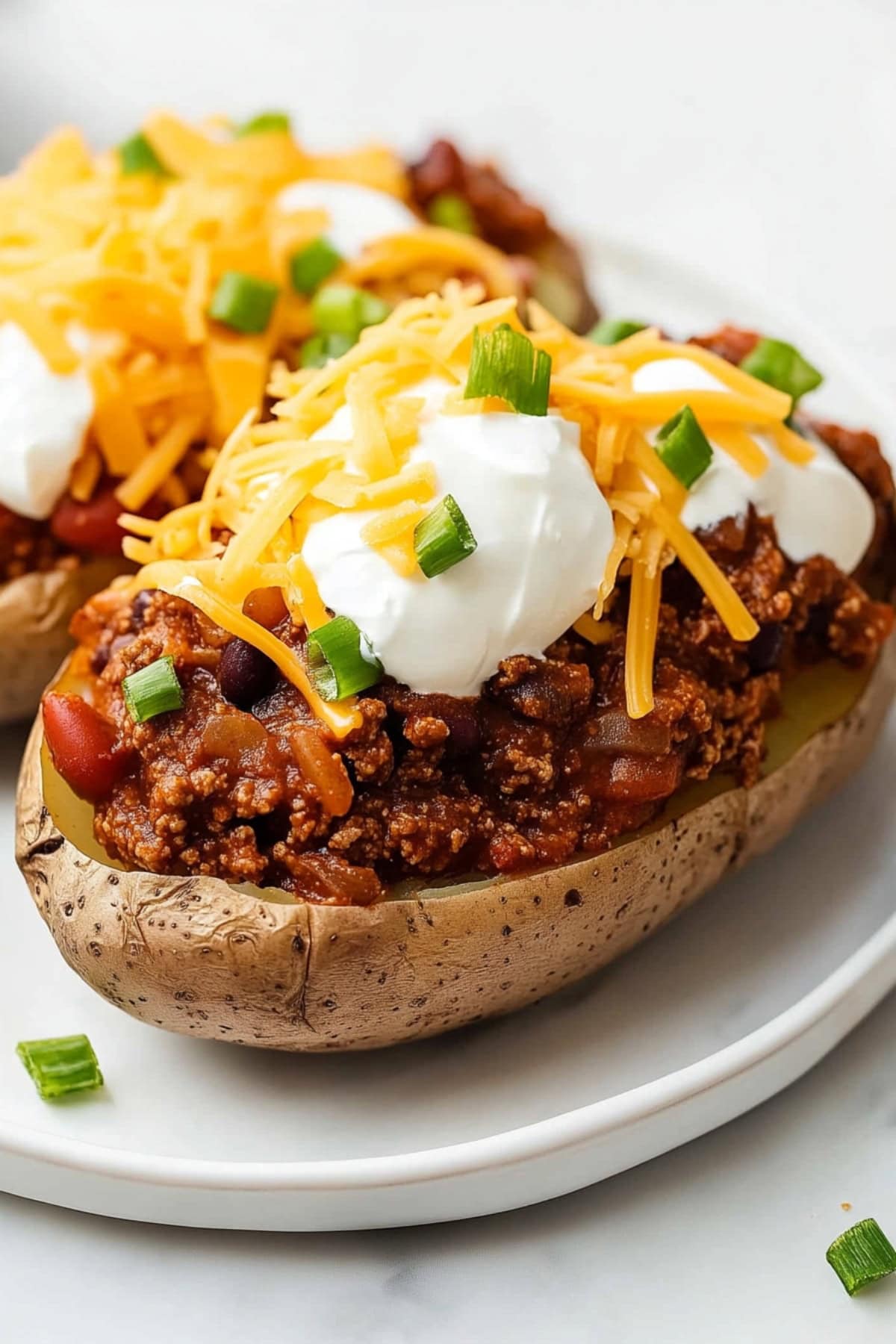 A plate of chili baked potatoes with ground beef, kidney beans, topped with sour cream and shredded cheese.