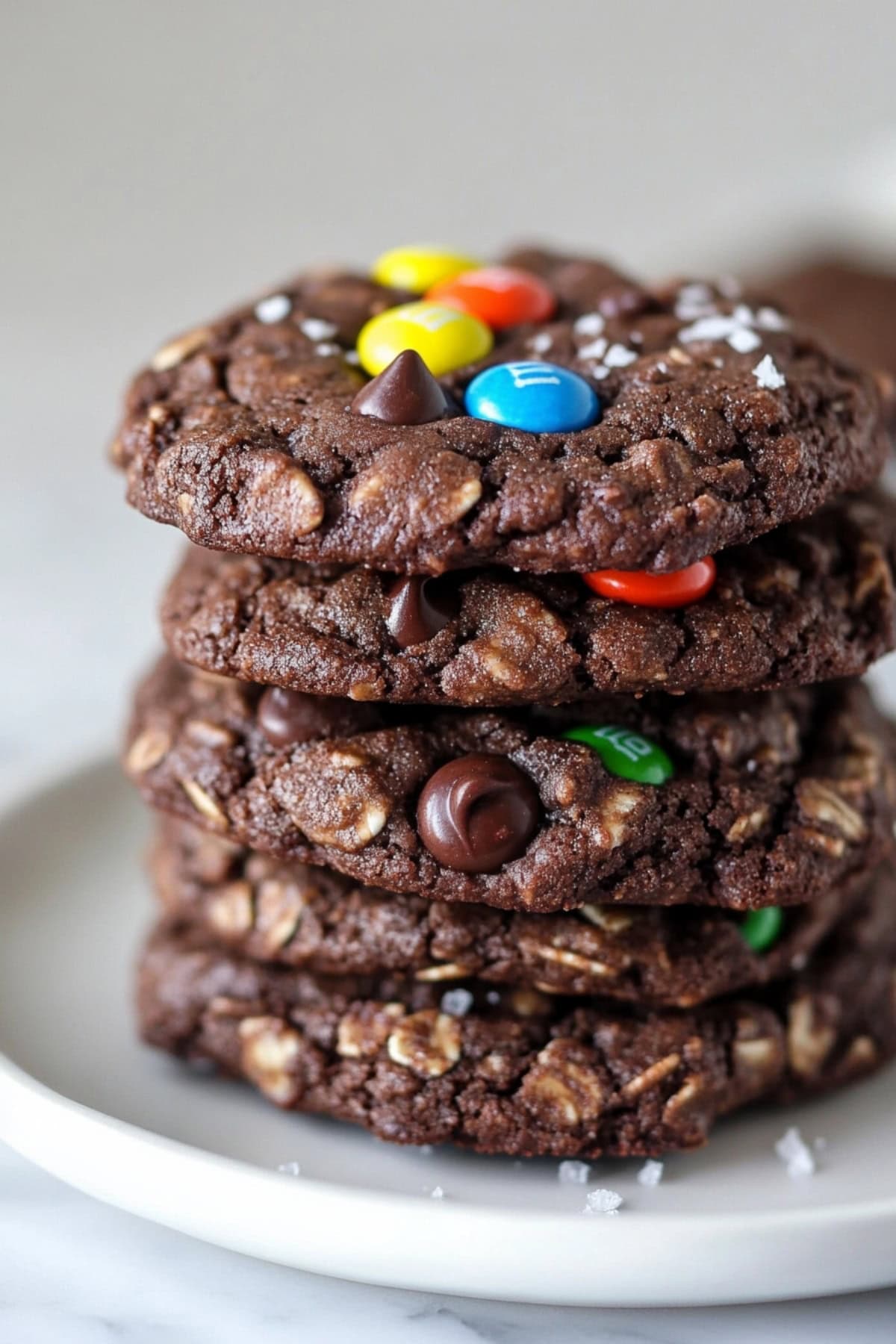 Chocolate monster cookies stacked on top of each other with M&Ms and chocolate chips on top.