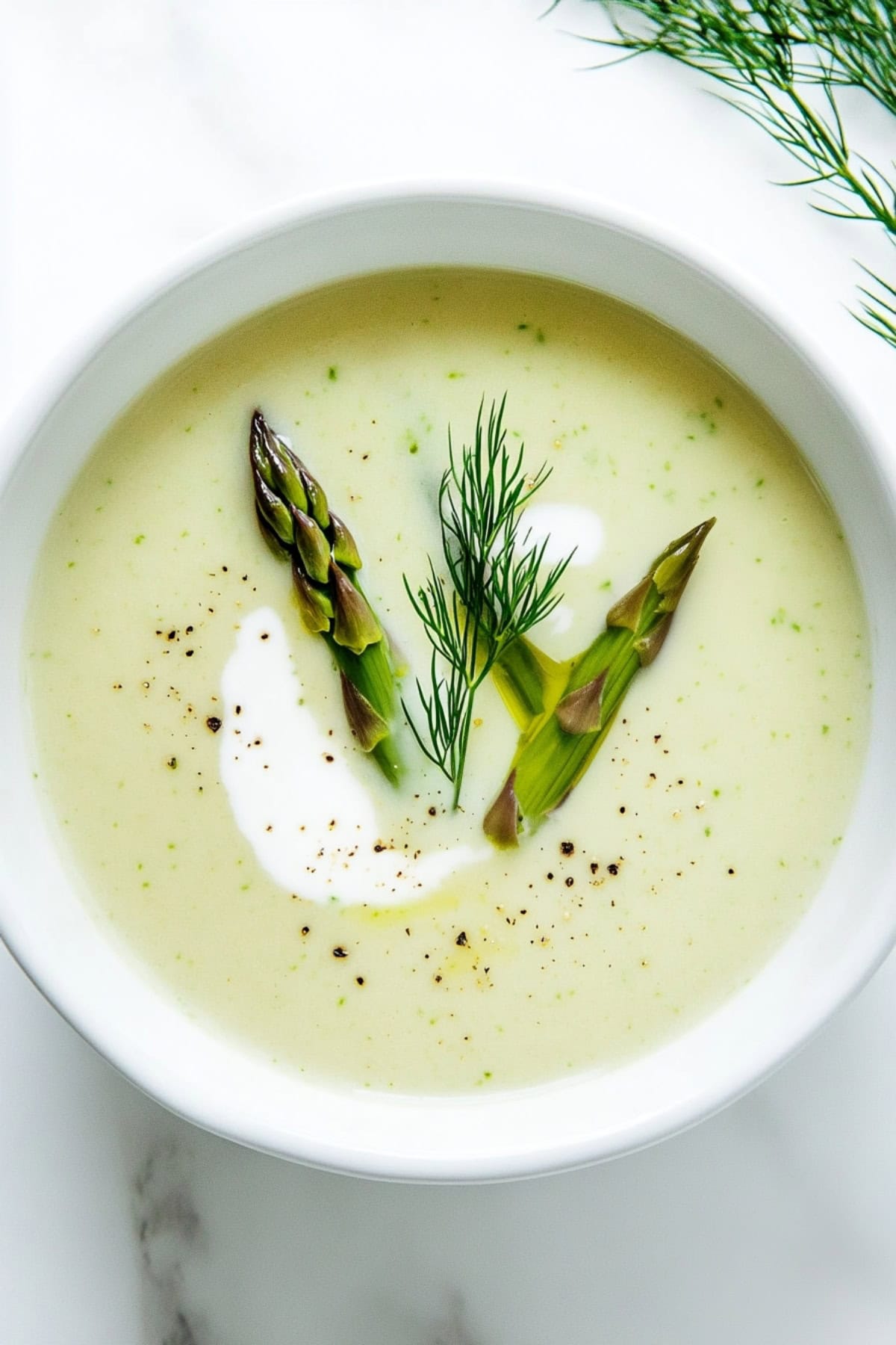 Creamy asparagus soup served in a white bowl garnished with asparagus and cream on top.