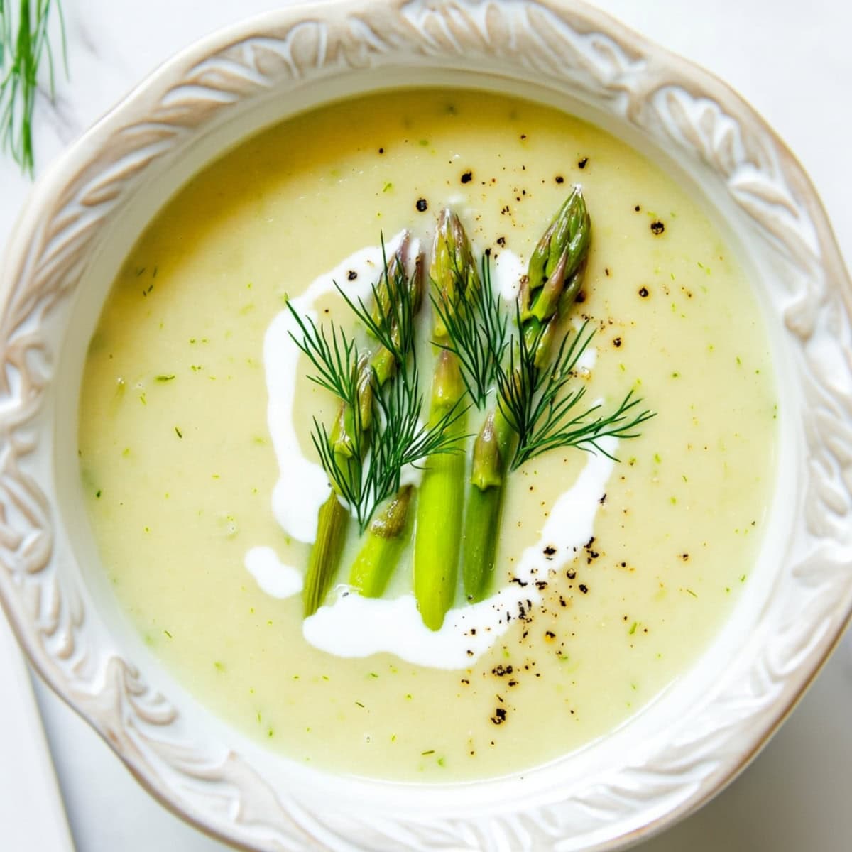 Cream of asparagus soup served in a white bowl garnished with asparagus slices and cream on top.