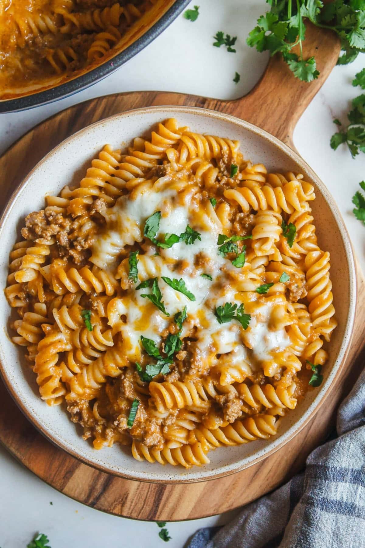 Serving of pasta with enchilada sauce with ground beef garnished with cheese and parsley served in a white plate.