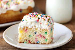 Moist and soft homemade funfetti poke cake in a plate, served with milk.