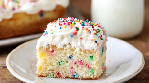 Moist and soft homemade funfetti poke cake in a plate, served with milk.