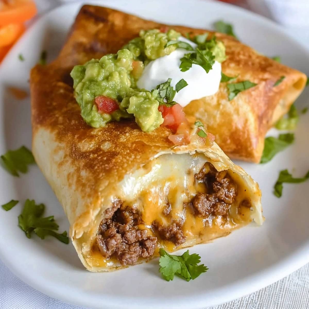 Beef and cheese chimichanga cut in half on a plate with guacamole, sour cream, and fresh cilantro. 