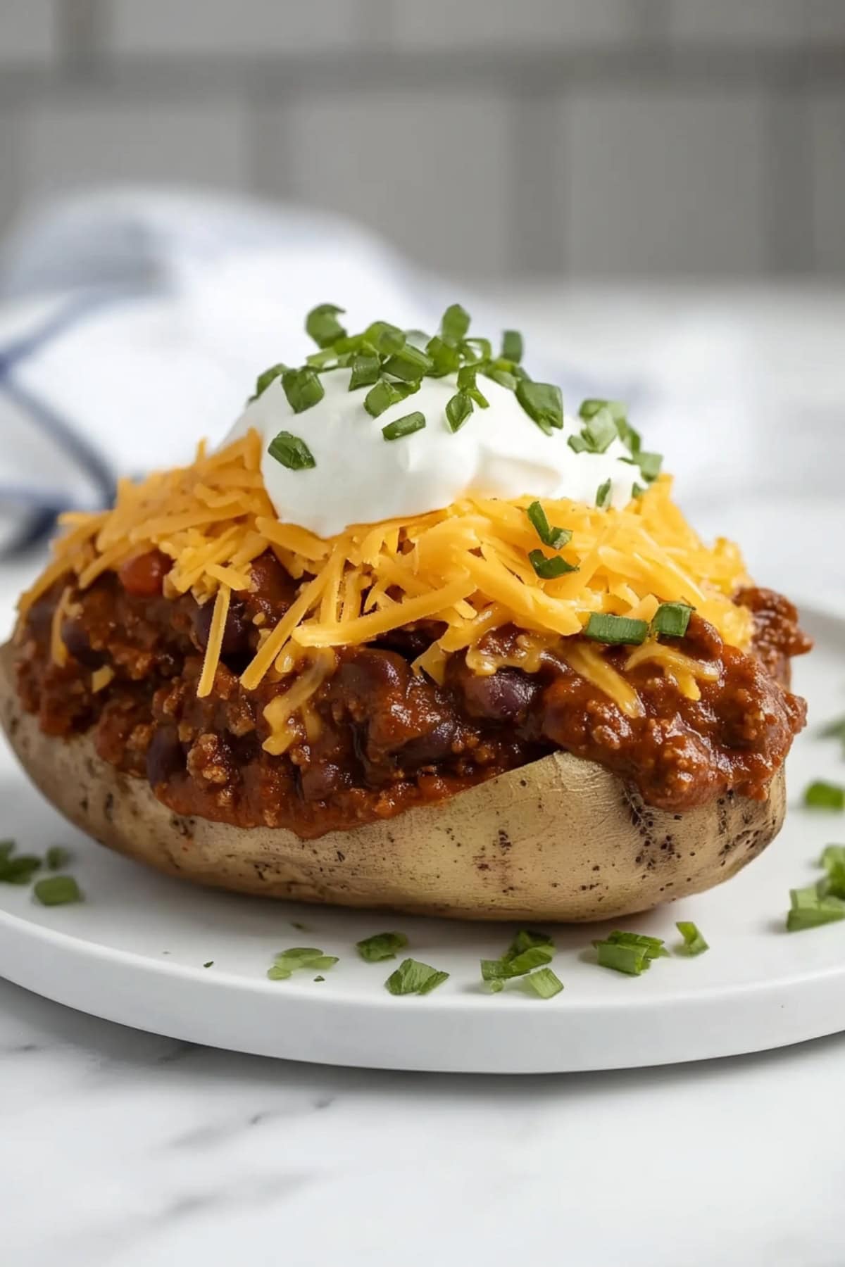 A rustic baked potato filled with rich chili, melted cheese, and garnished with green onions and sour cream.