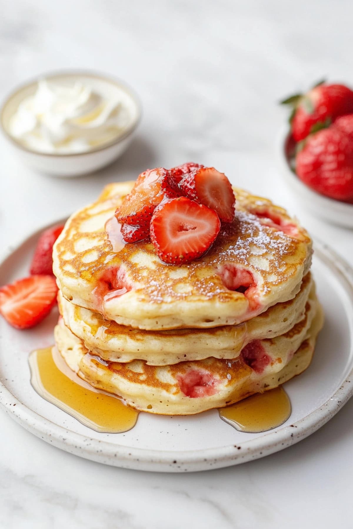 Stack of warm pancakes covered in strawberry slices and a drizzle of maple syrup