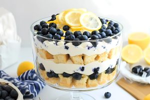 Lemon blueberry trifle arranged inside a large trifle glass garnished with blueberries and lemon slices.