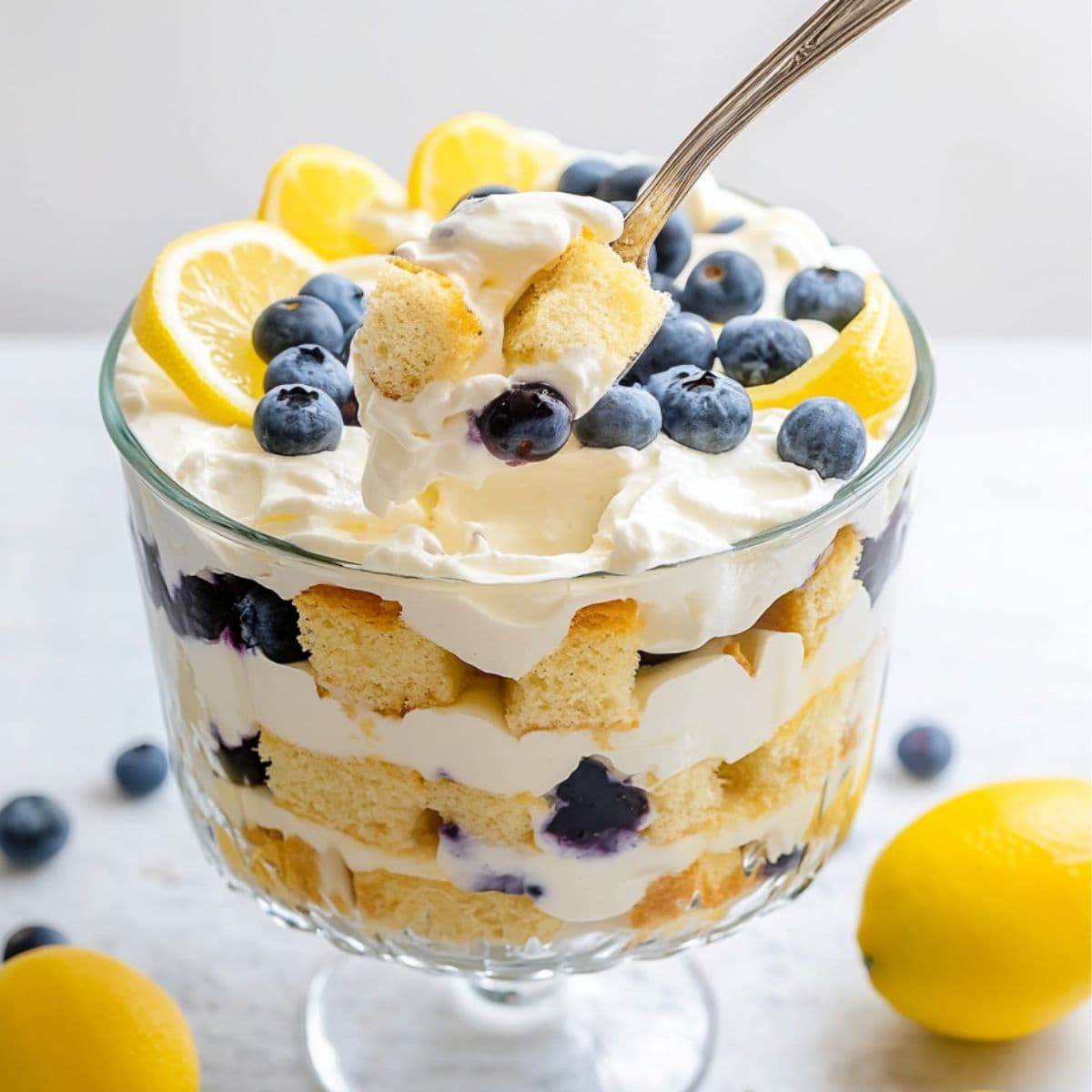 Large spoon scooping a serving from lemon blueberry trifle inside a large trifle glass. 