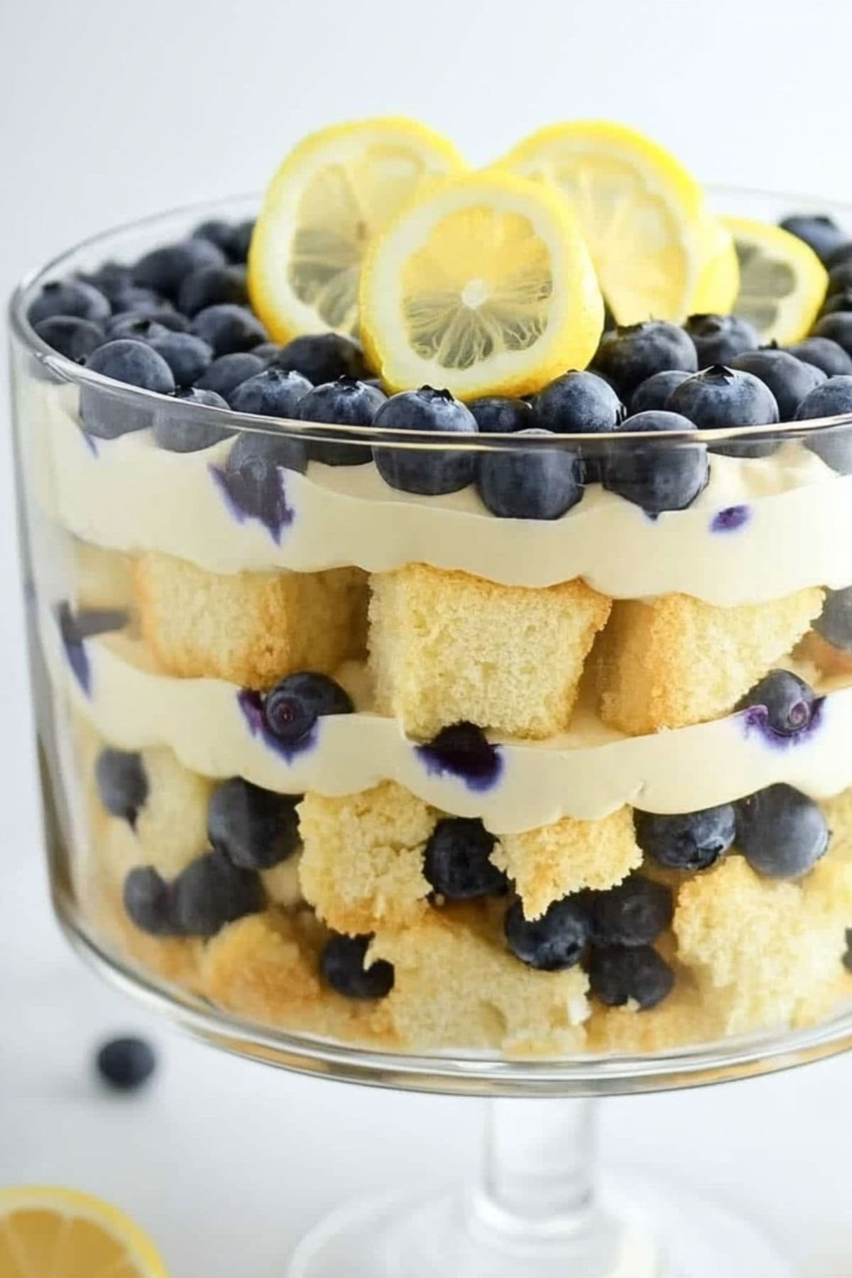 Layered cake cube slices, lemon pudding and blueberries in a large glass trifle glass. 