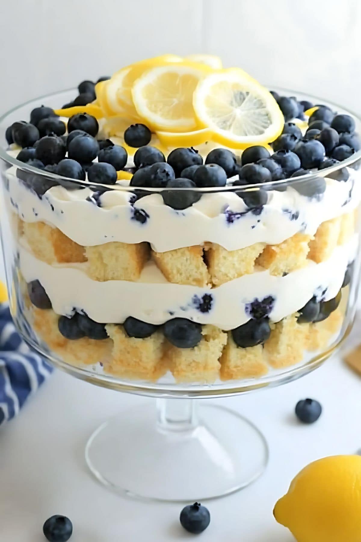 Large glass trifle with layers of angel cube cake, lemon pudding and blueberries.