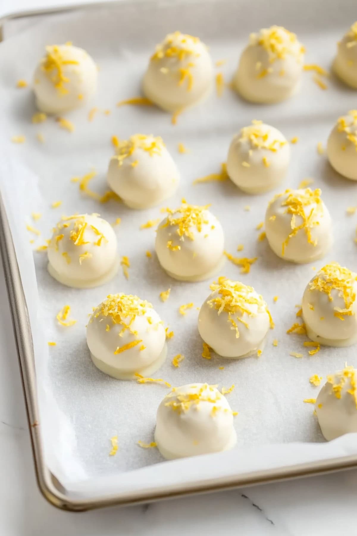 Lemon oreo truffles sitting on top of parchment paper in a baking sheet.