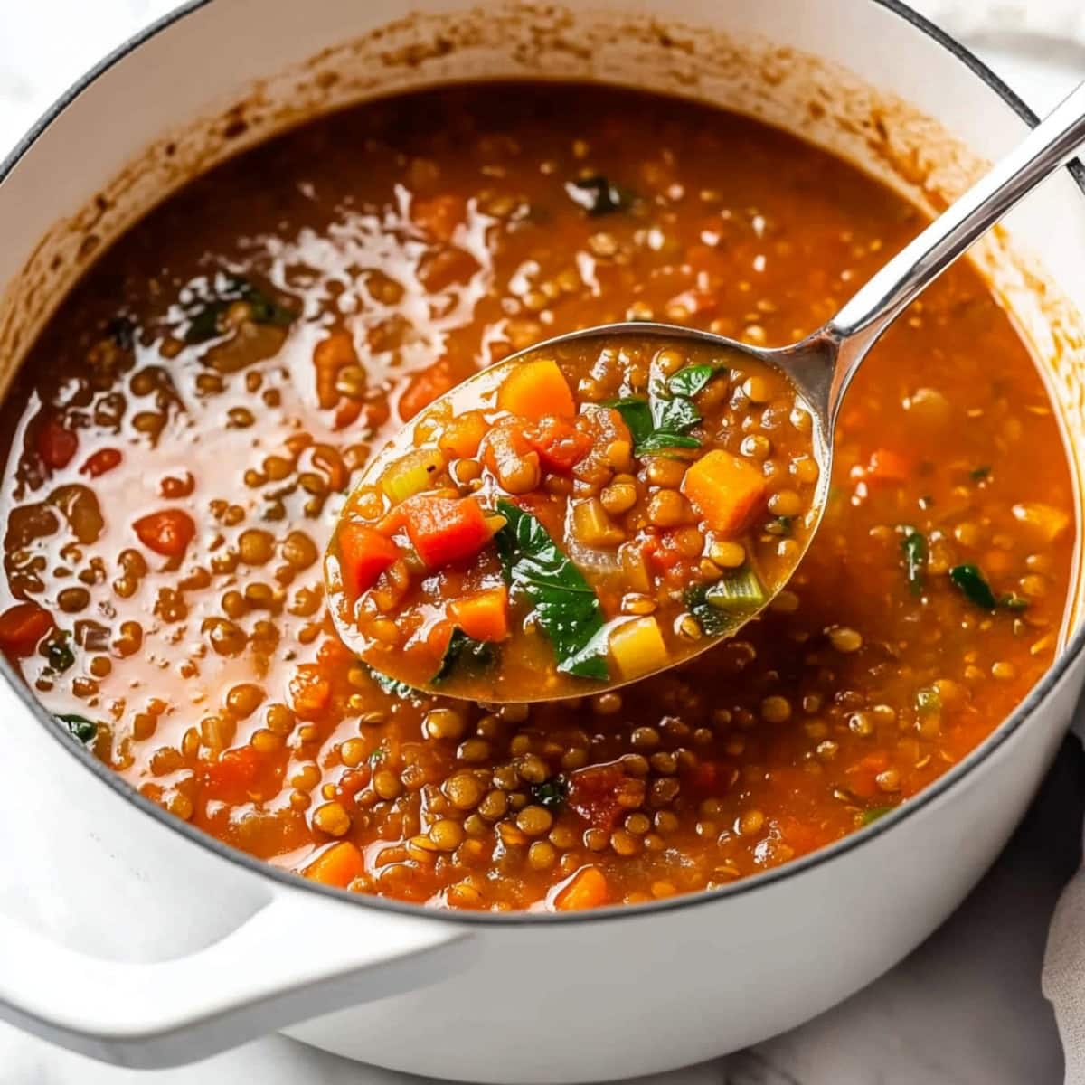 A spoonful of lentil soup with carrots,  tomatoes and spinach.