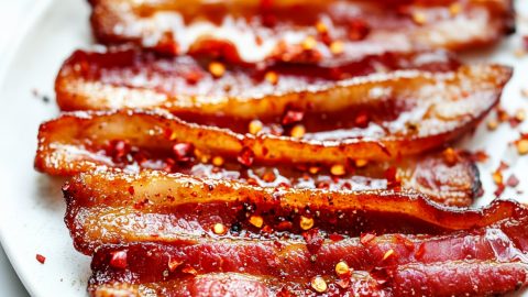 Million dollar bacon with sugar and maple syrup sprinkled with pepper flakes served in a white plate.