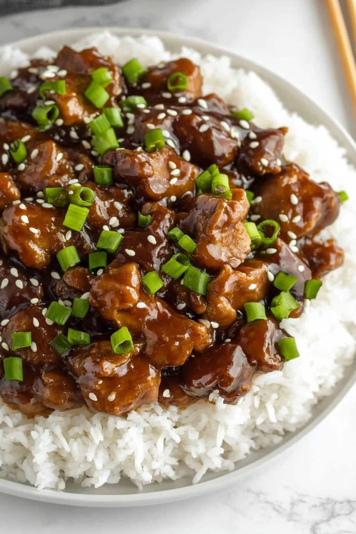 White rice topped with sauce Mongolian pork garnished with sesame seeds and chopped onions.