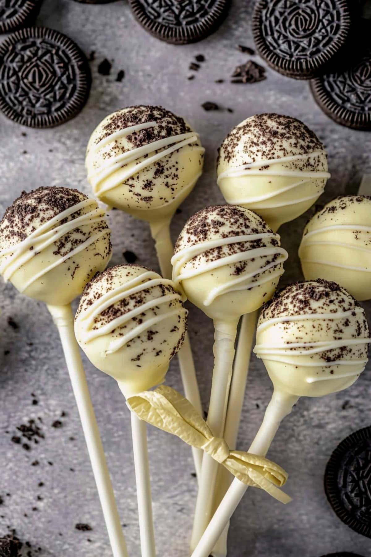 Bunch of white chocolate coated cake pops tied on stick lying on a concrete table.