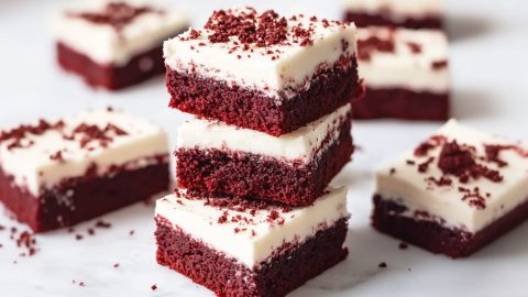 Sliced red velvet bars with cream cheese frosting stacked on a white marble table
