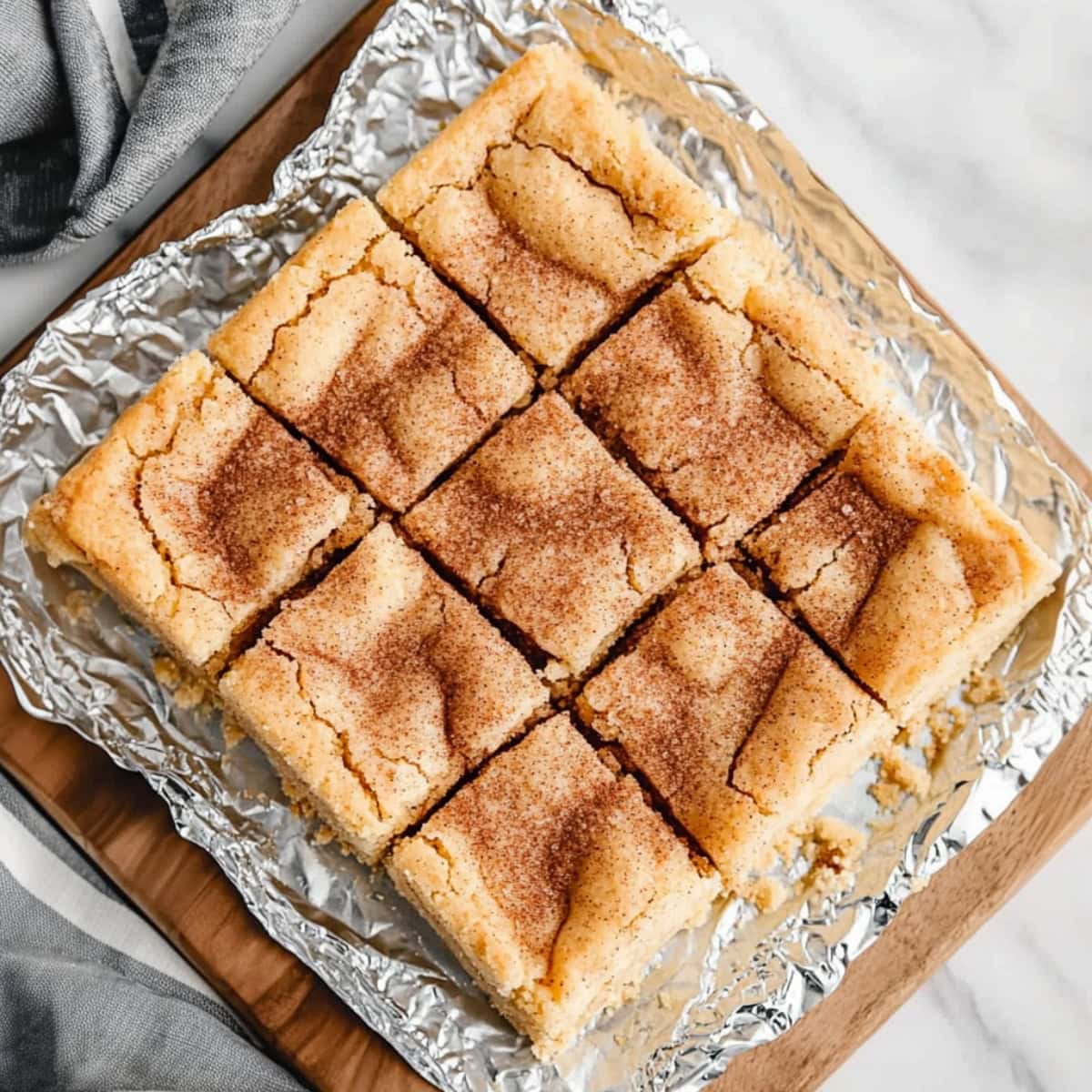 Sliced snickerdoodle cheesecake bar sitting on a wooden board on top of aluminum foil.