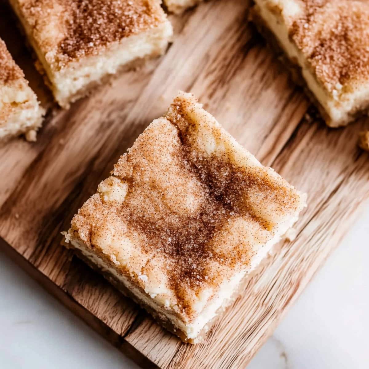 Snickerdoodle cheesecake bars sitting on top of wooden board.