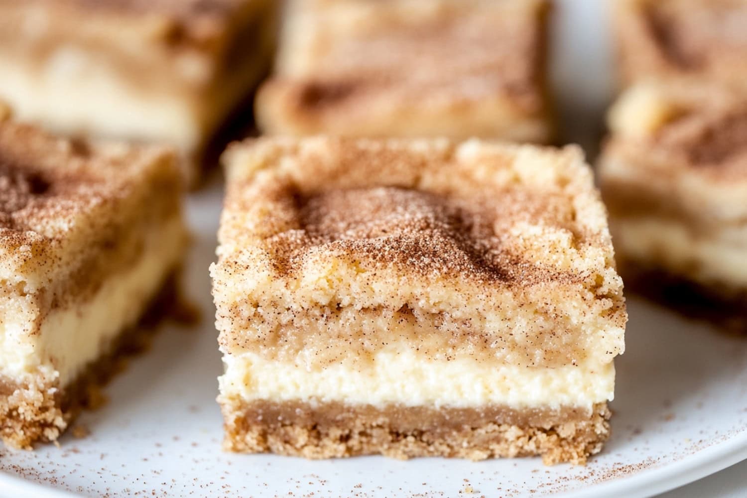 Snickerdoodle cheesecake bars slices sitting on whtie plate.