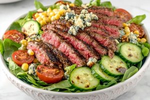 A delicious steak salad with vegetables, blue cheese, corn and dijon mustard dressing in a bowl.