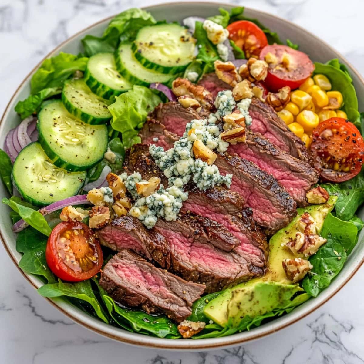 A bowl of homemade steak salad with sliced cucumber, tomatoes, blue cheese and nuts.