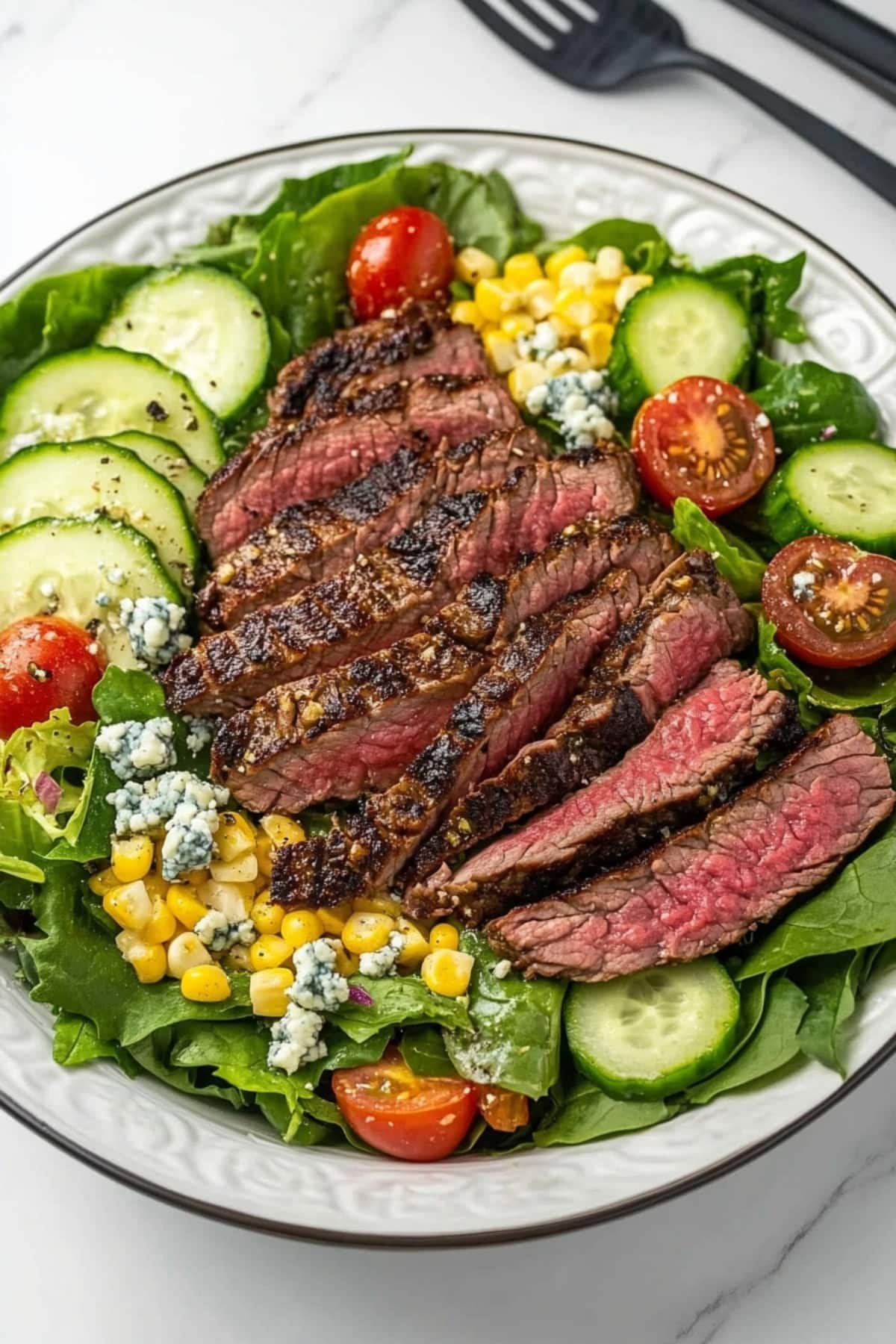 An overhead view of steak salad with corn, blue cheese, tomatoes and cucumbers.