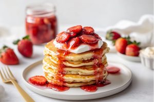 Pancakes topped with strawberries, sauce and whipped cream in a plate.