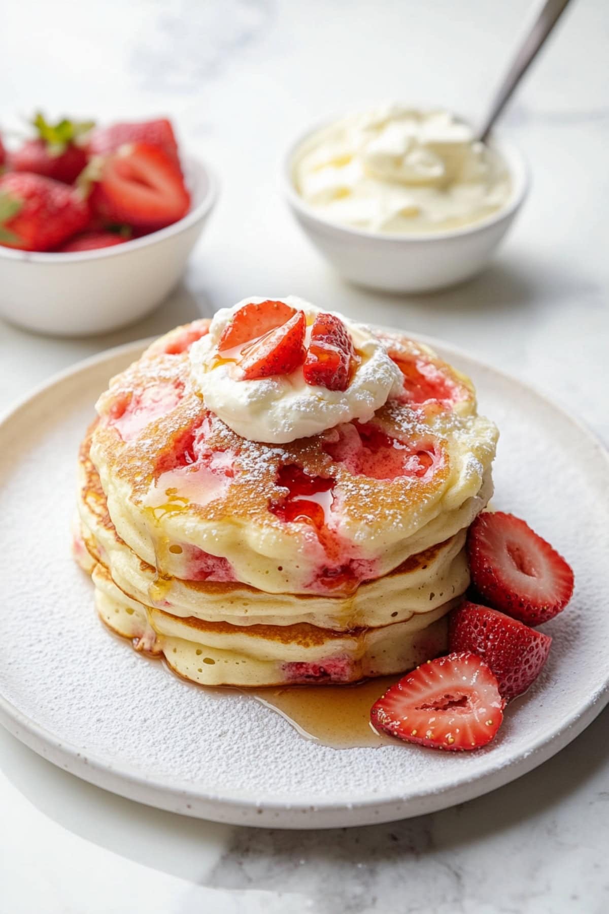 A plate of fluffy pancakes with whipped cream, powdered sugar, and strawberries.