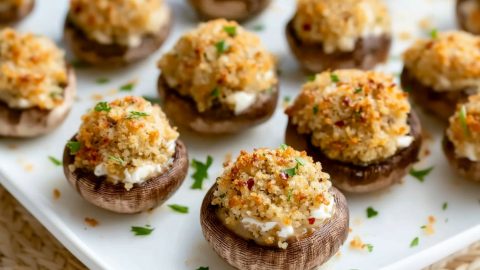 Cheese stuffed cremini mushrooms covered with breadcrumbs arranged in a white plate.