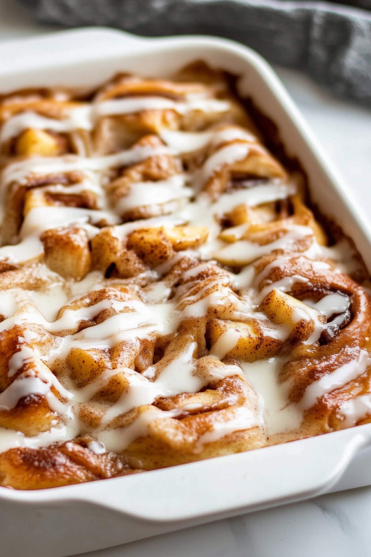 A baking dish filled with apple cinnamon rolls, drizzled with glaze.