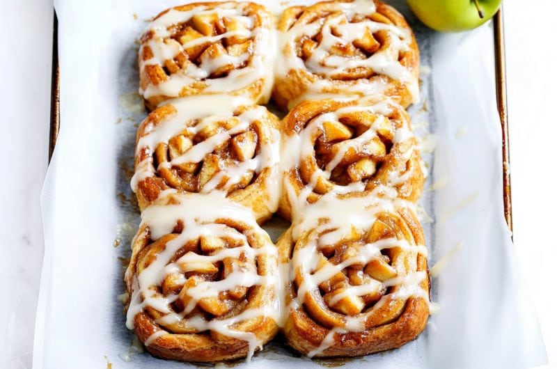 A baking pan of apple pie cinnamon rolls with sweet glaze.