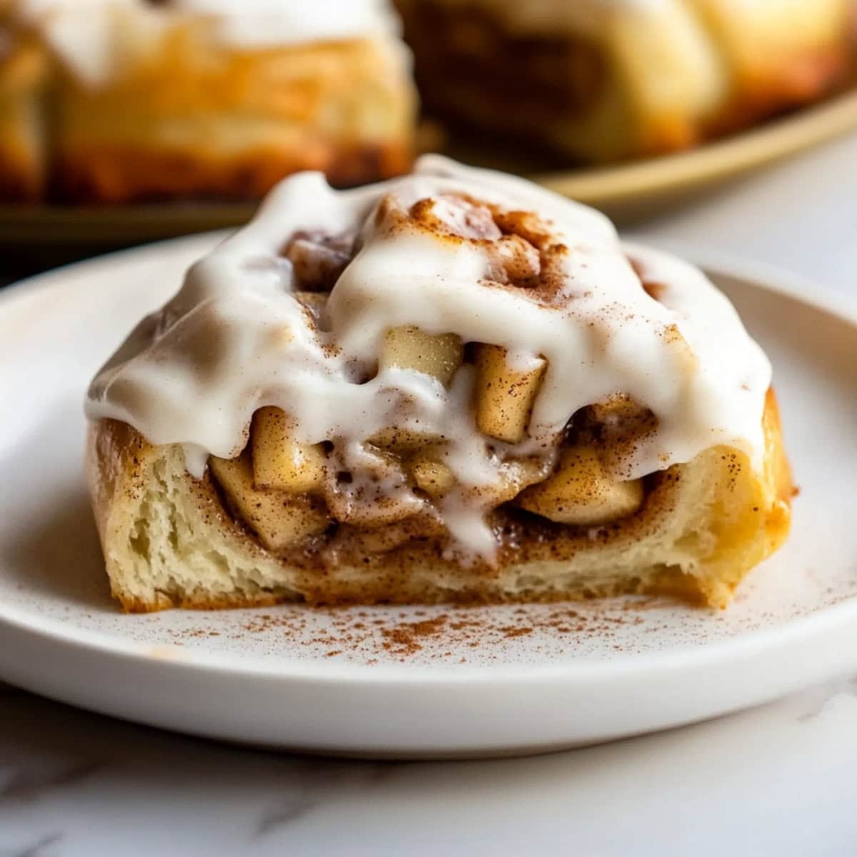 An apple pie cinnamon roll with glaze, cut in half on a plate.